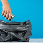 A person throwing trash in a black colored plastic bag