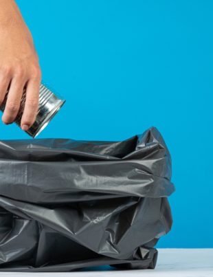 A person throwing trash in a black colored plastic bag
