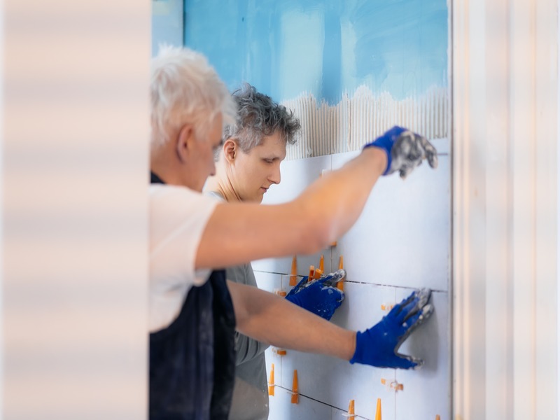 Individuals remodeling a bathroom by installing new wall tiles to create a modern bathroom design.